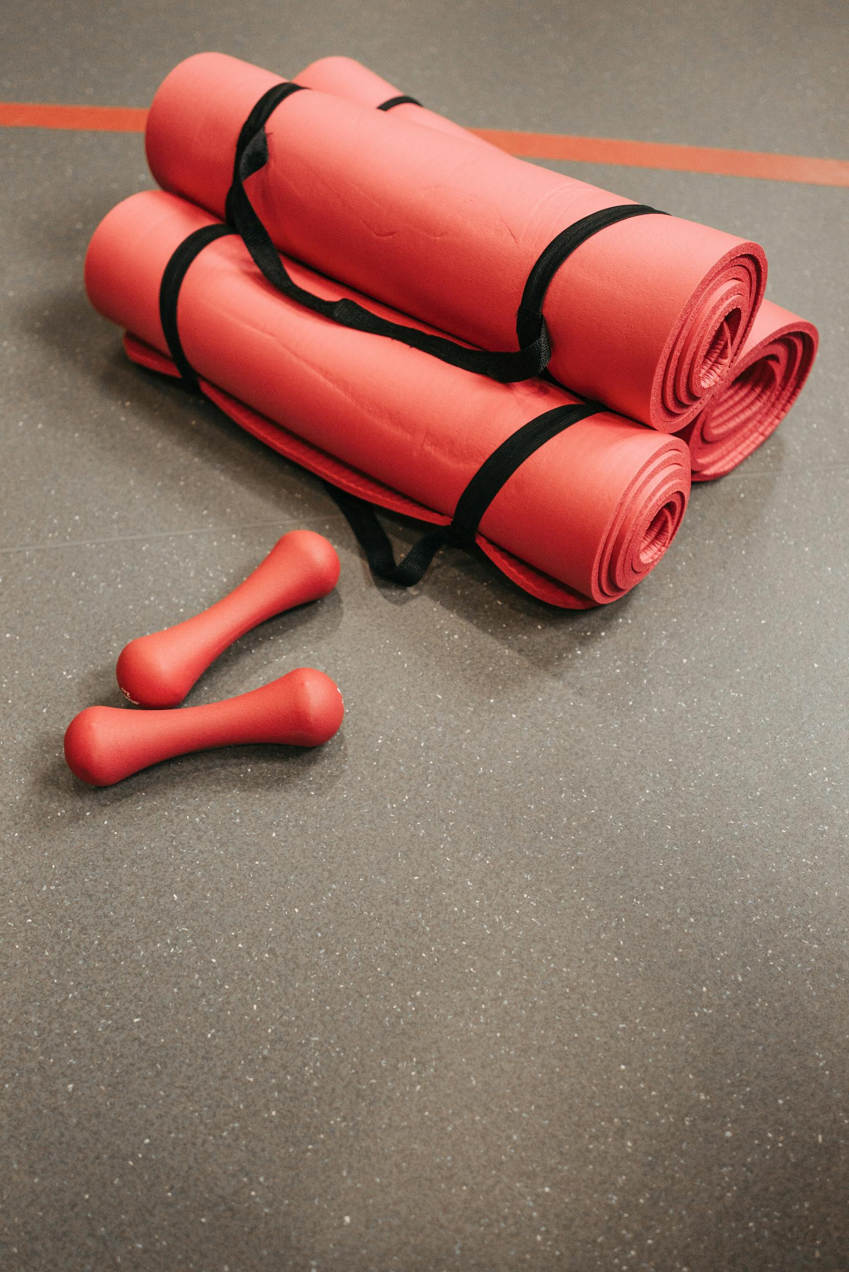 Red yoga mats and dumbbells placed on a gym floor, ideal for fitness and exercise themes.